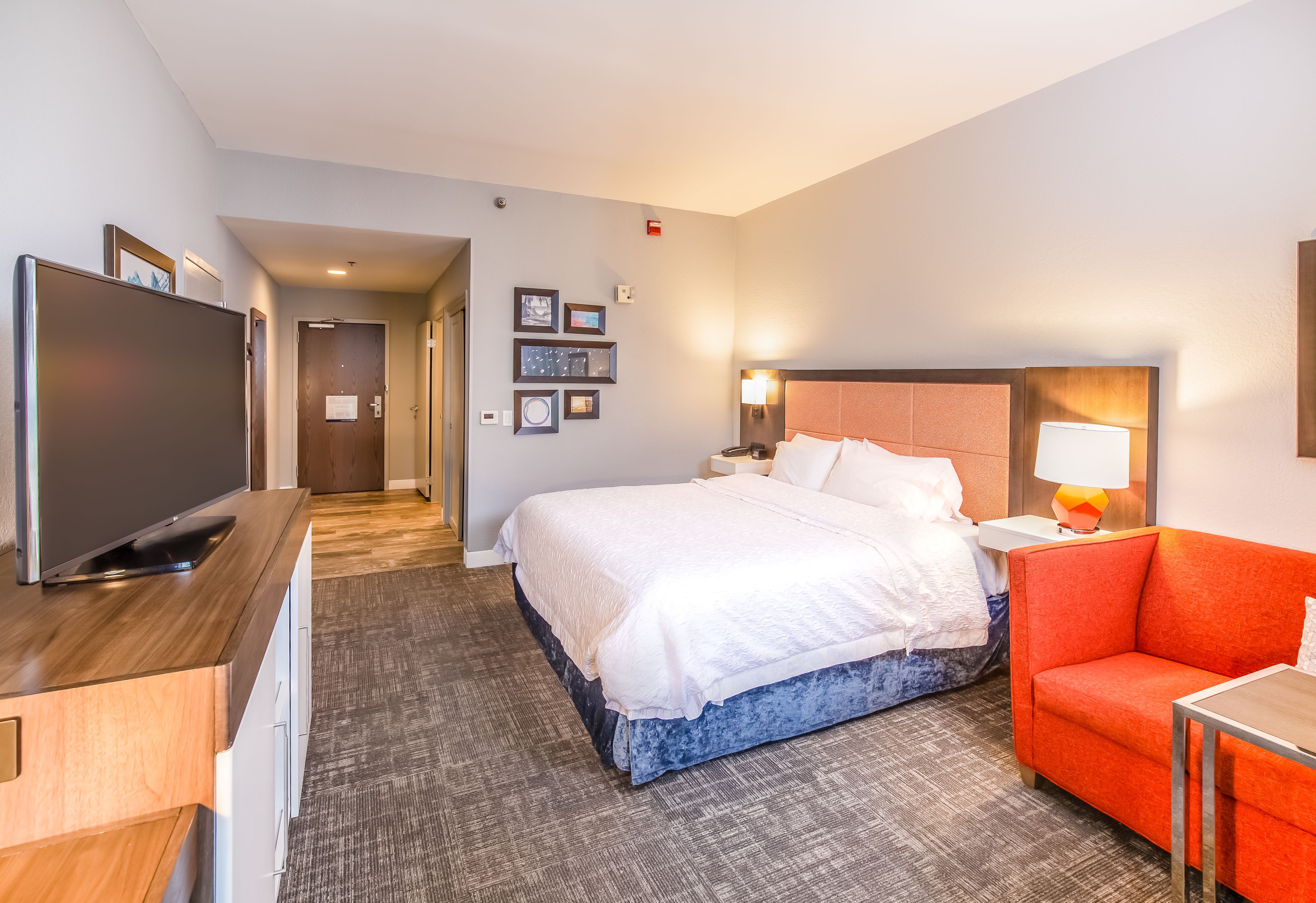 Habitación de hotel con una cama grande, televisión, escritorio y un sillón rojo.