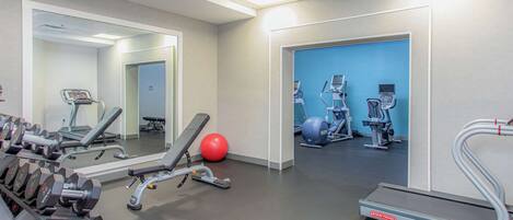 Un gimnasio con diversos equipos de ejercicio, incluyendo mancuernas, una cinta de correr y pelotas de ejercicio.