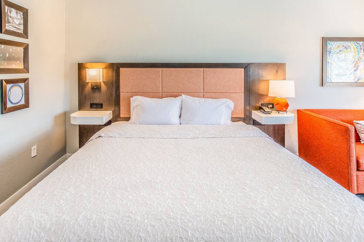 A hotel room with a large bed, two bedside tables with lamps, a headboard, and framed pictures on the wall.
