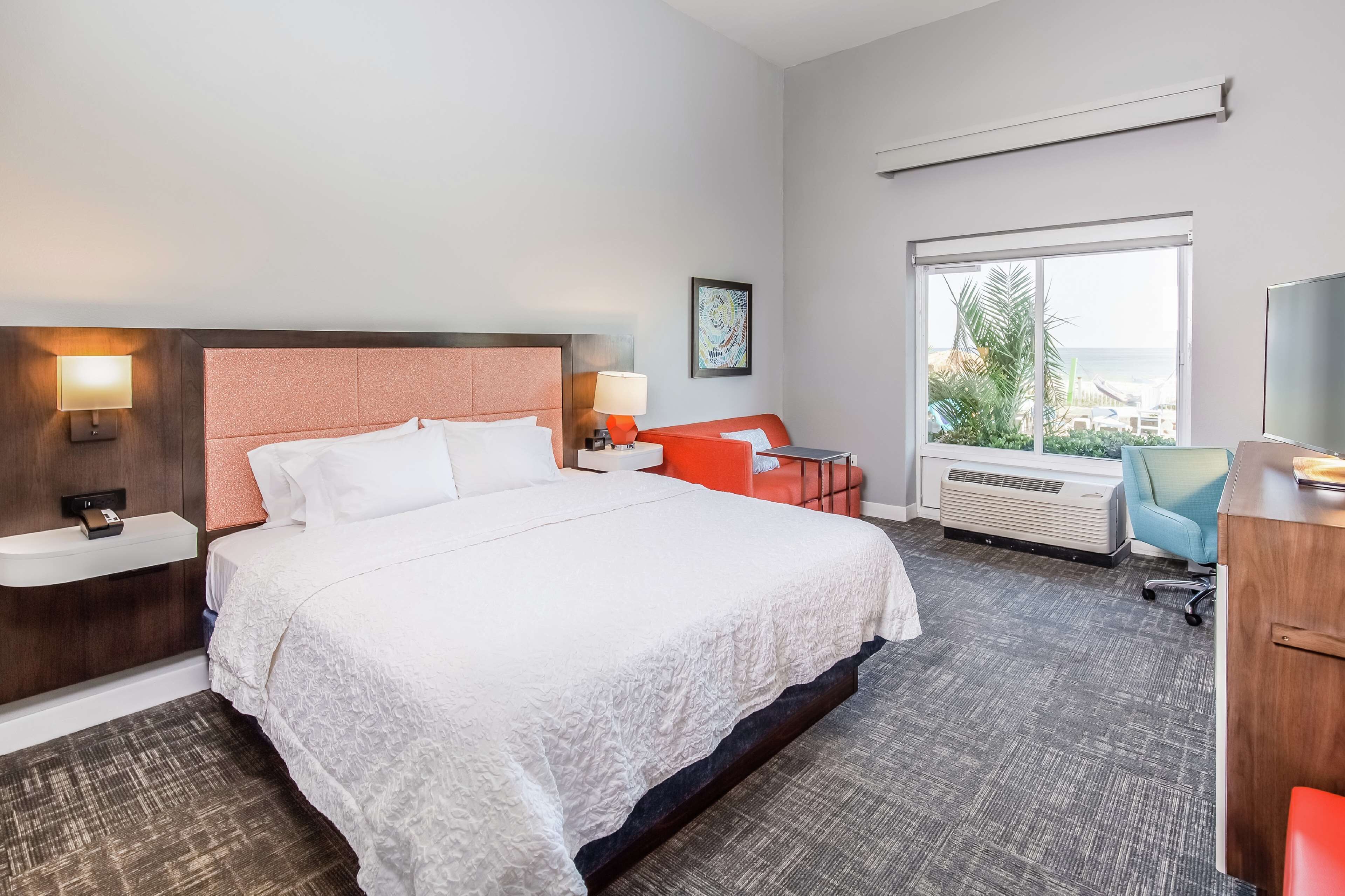 A hotel room with a large bed, a desk, a chair, a TV, and a window with a view of the outdoors.