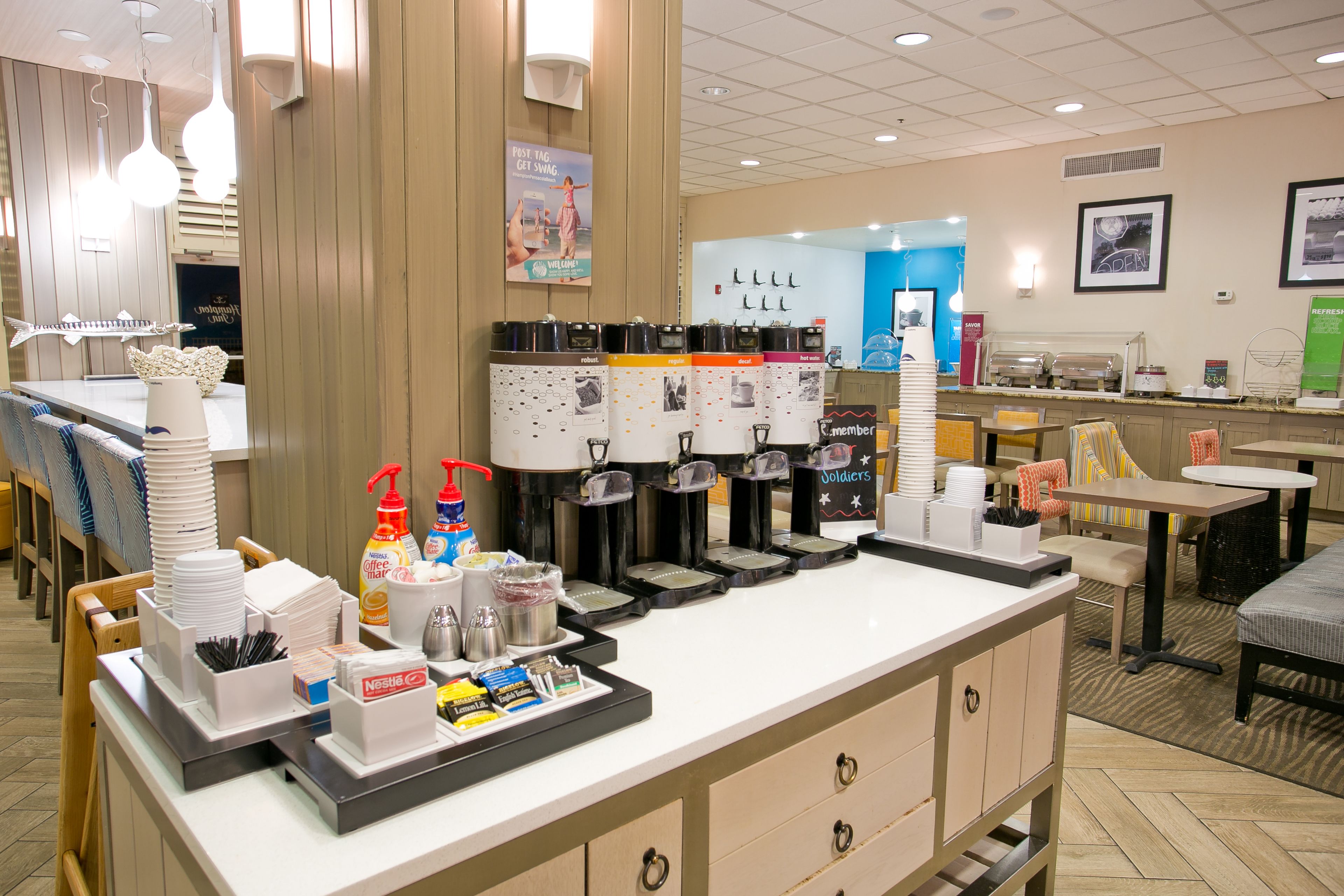 Una zona de cafè amb diverses cafeteres, un dosificador de begudes i una varietat de tasses i mugs.