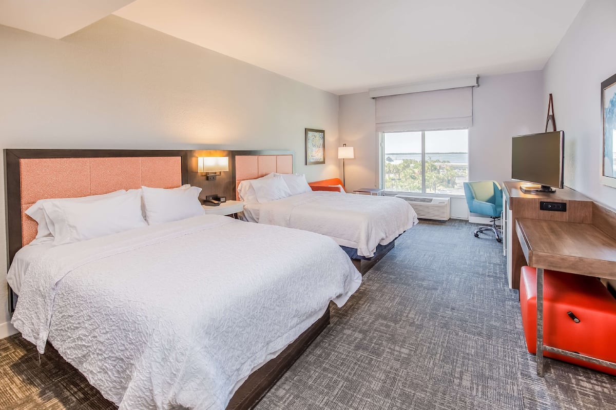 A hotel room with two beds, a desk, a chair, a TV, and a window with a city view.