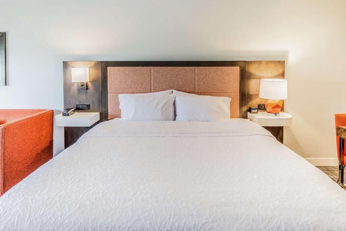 A hotel room with a large bed, two bedside tables, a nightstand, a lamp, and a chair.