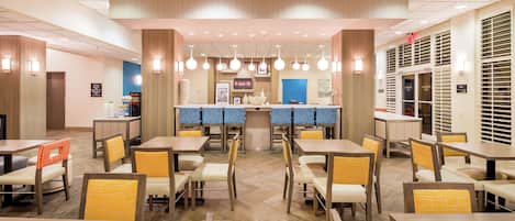Moderni ravintola, jossa on keskeisellä paikalla sijaitseva baaritiskialue, useita pöytiä ja tuoleja, joissa on keltaiset tyynyt.
