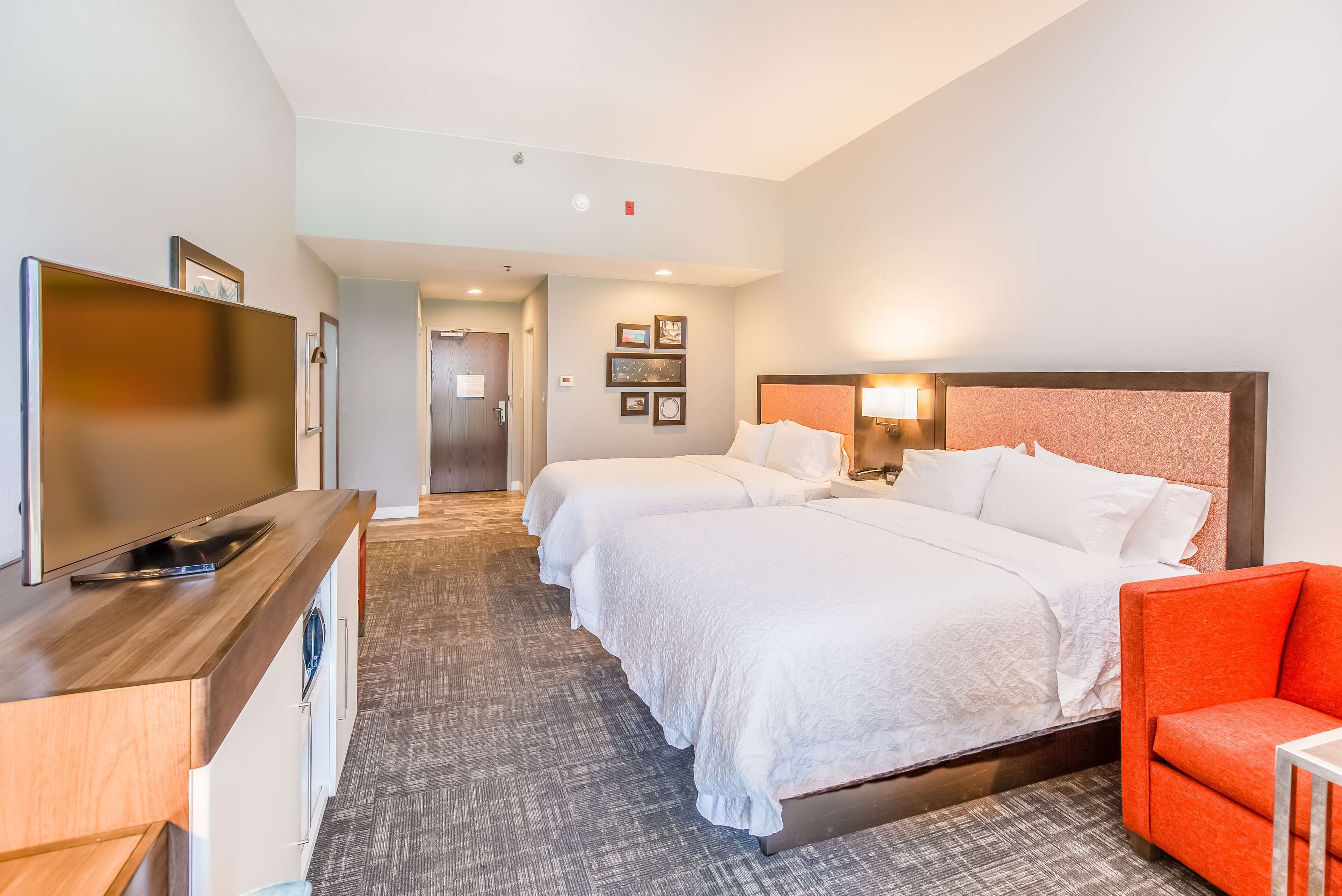 A hotel room with a large bed, a TV, a desk, and a red chair.