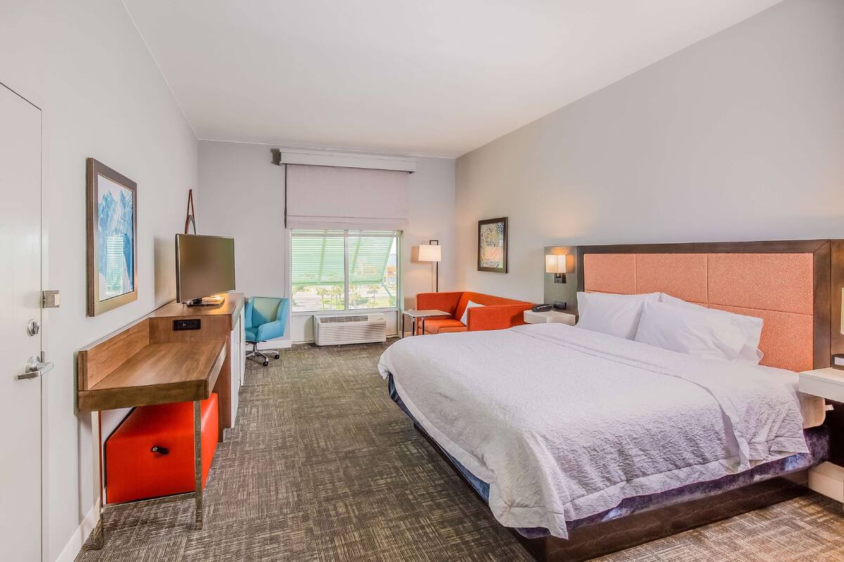 A hotel room with a bed, desk, chair, and a window with blinds.