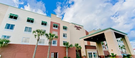 A Hampton Inn hotel with a two-story building, a covered entrance, and palm trees in the landscaping.