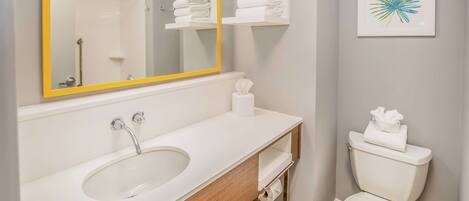 A bathroom with a white sink, a mirror with a yellow frame, a toilet, and a towel rack with folded towels.