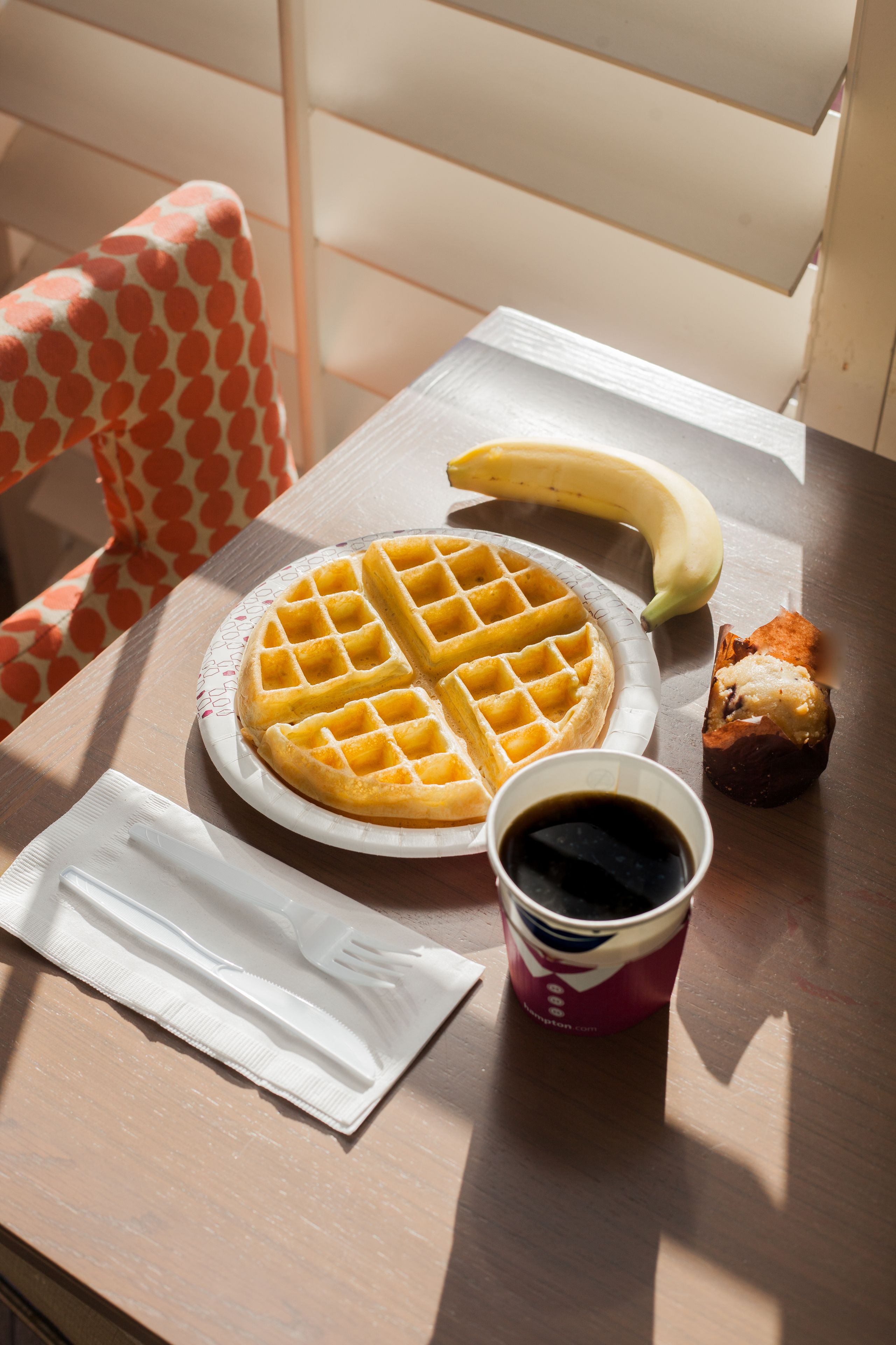 A table with a waffle, a banana, a piece of toast, and a cup of coffee.
