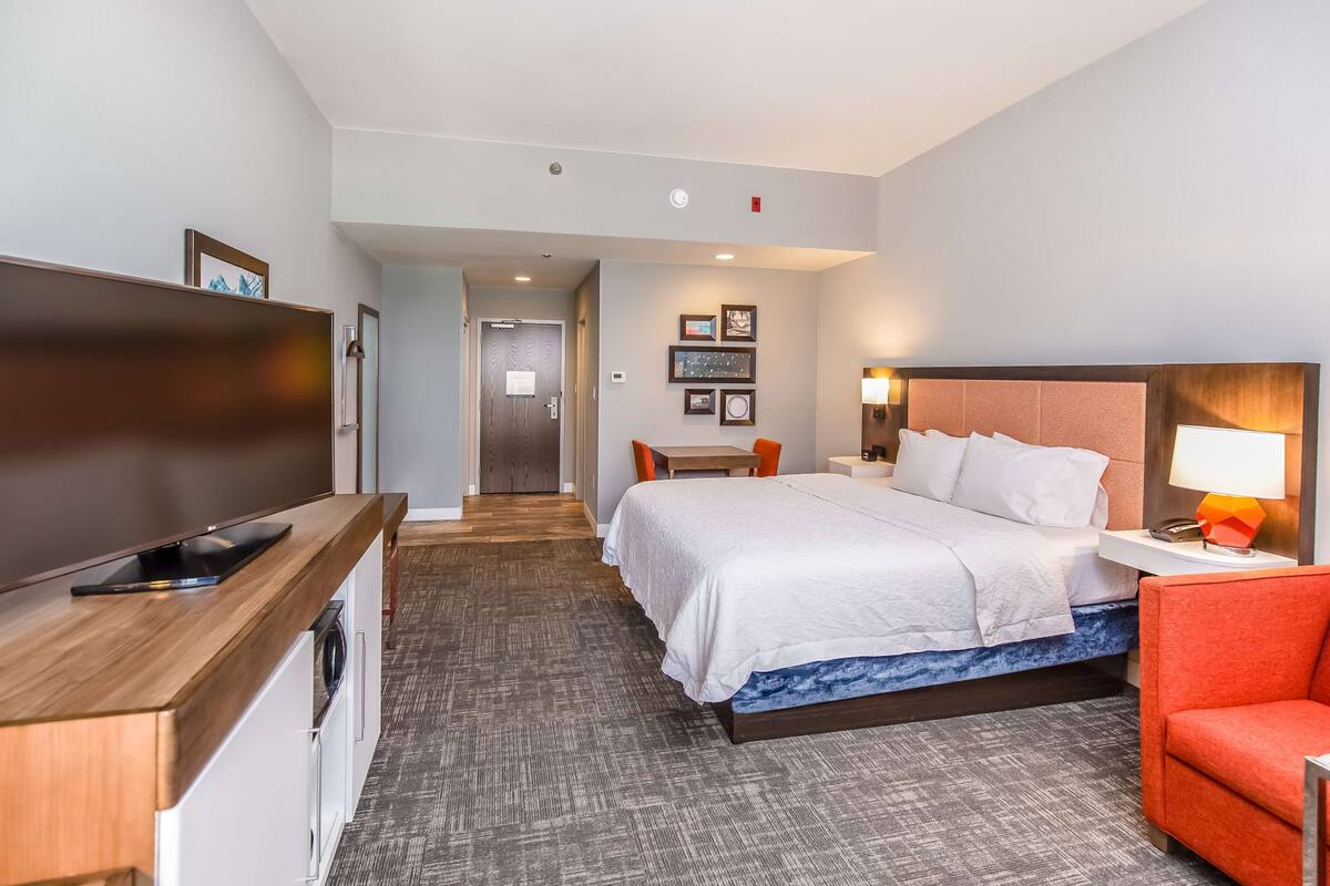A hotel room with a bed, a desk, a chair, a TV, and a washing machine.