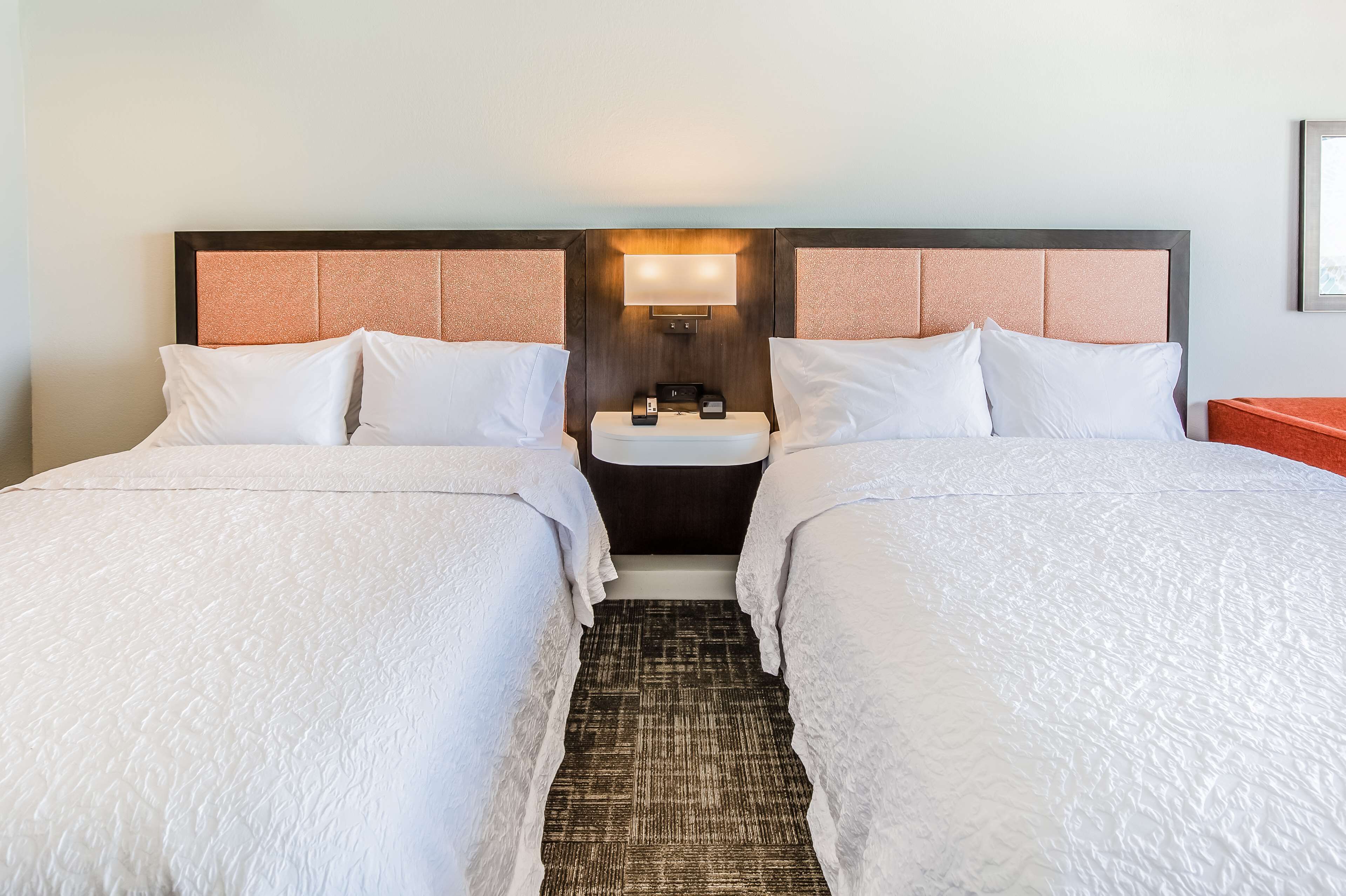 A hotel room with two beds, a nightstand with a lamp, and a small sink.
