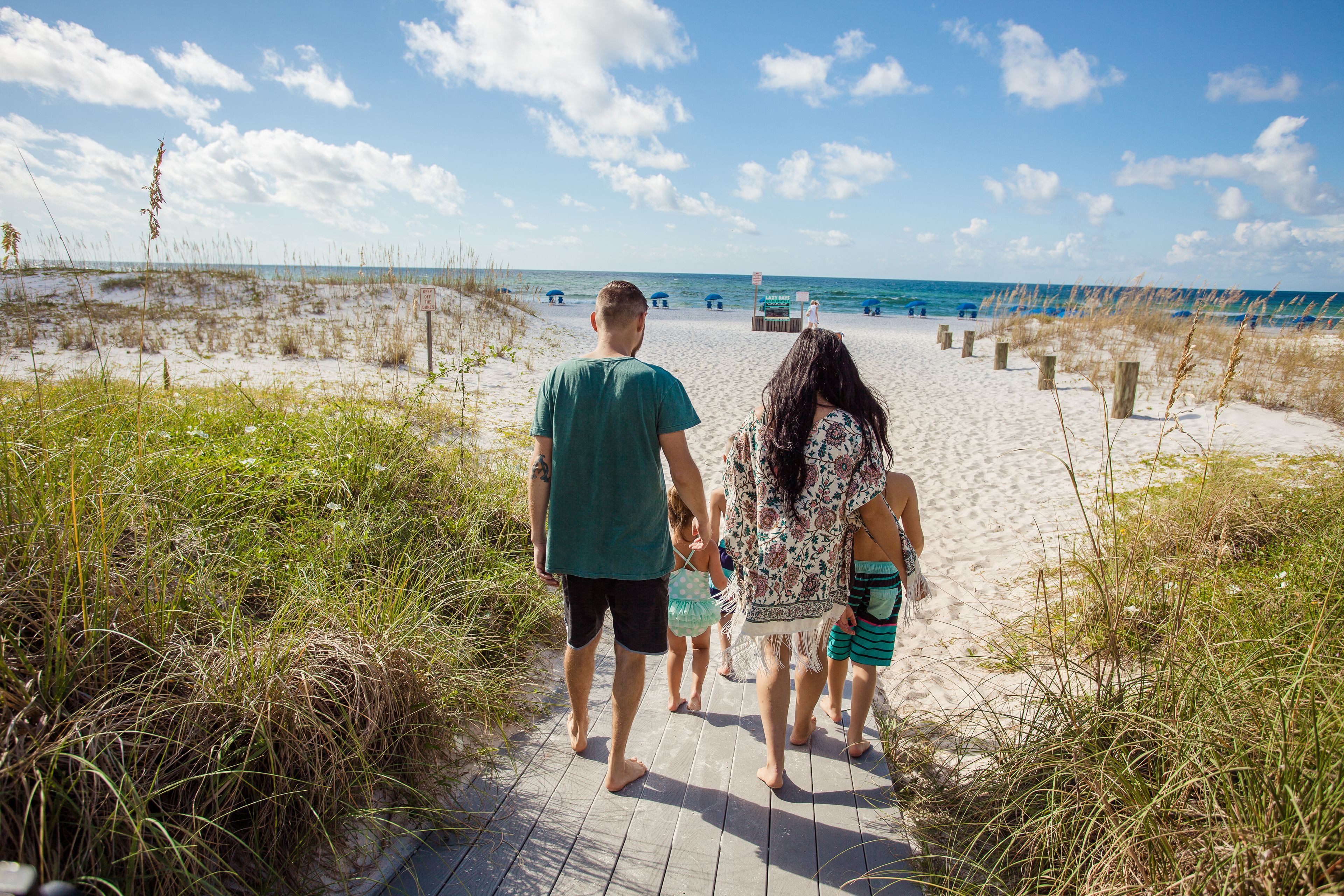 A pathway leading to a beach with sand and sparse vegetation.