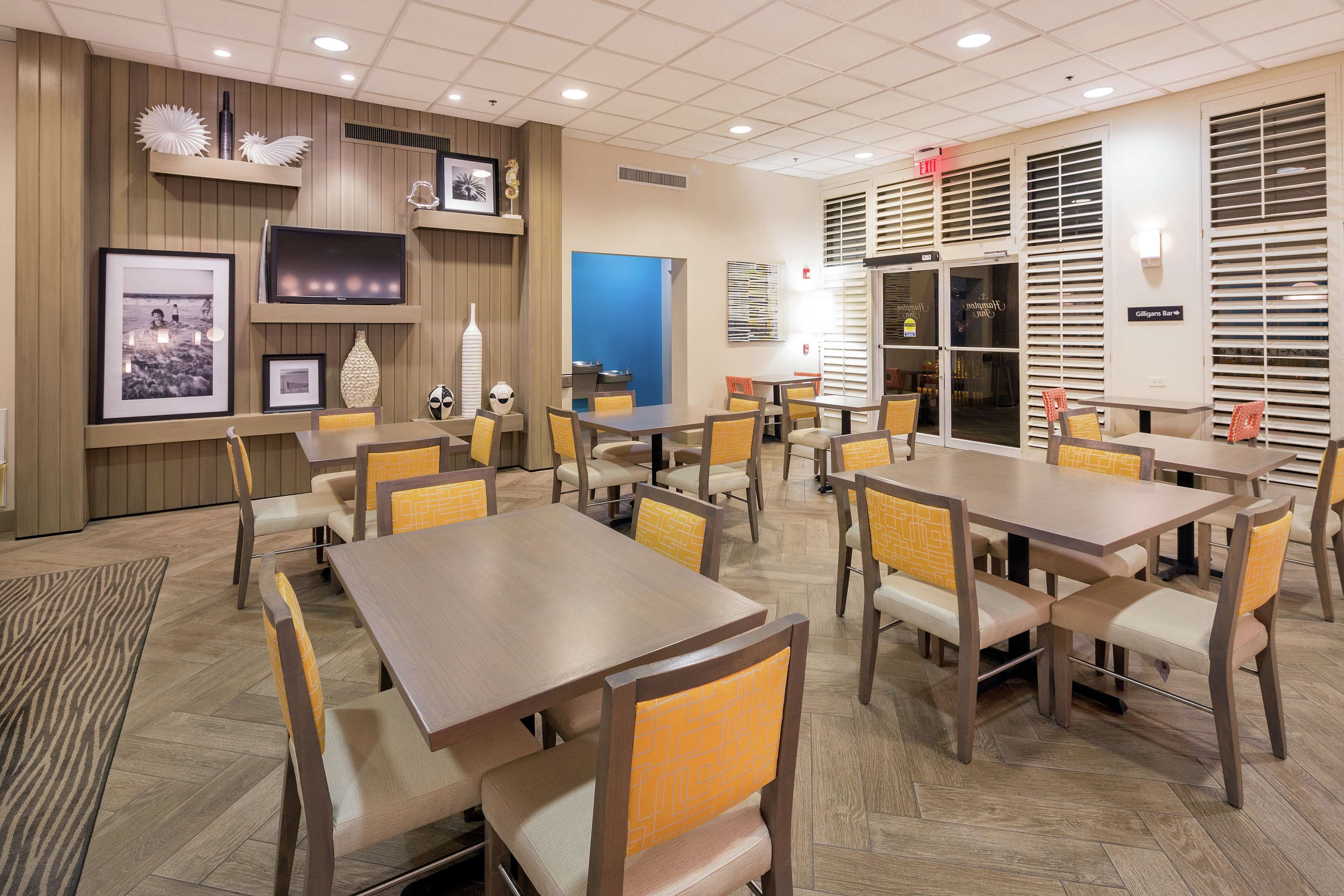 A hotel dining area with multiple tables and chairs, framed pictures on the walls, and a blue accent wall.