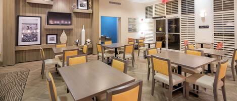 A hotel dining area with multiple tables and chairs, framed pictures on the walls, and a blue accent wall.
