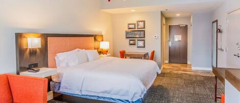 A hotel room with a large bed, a desk, a chair, and a small table.