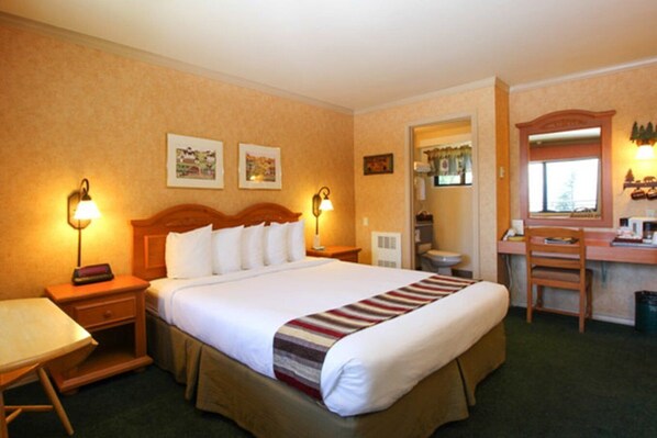 Una habitación de hotel con cama, mesitas de noche, escritorio, silla y espejo.