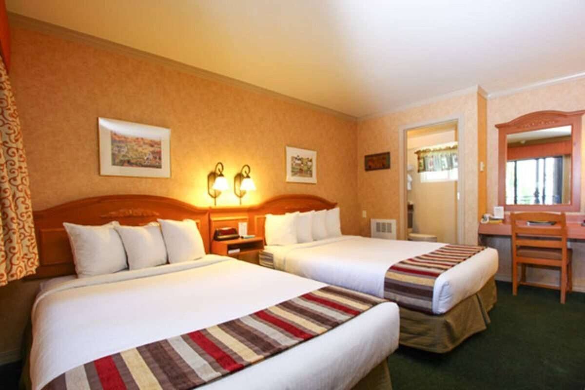 A hotel room with two beds, a desk, a chair, and a mirror.