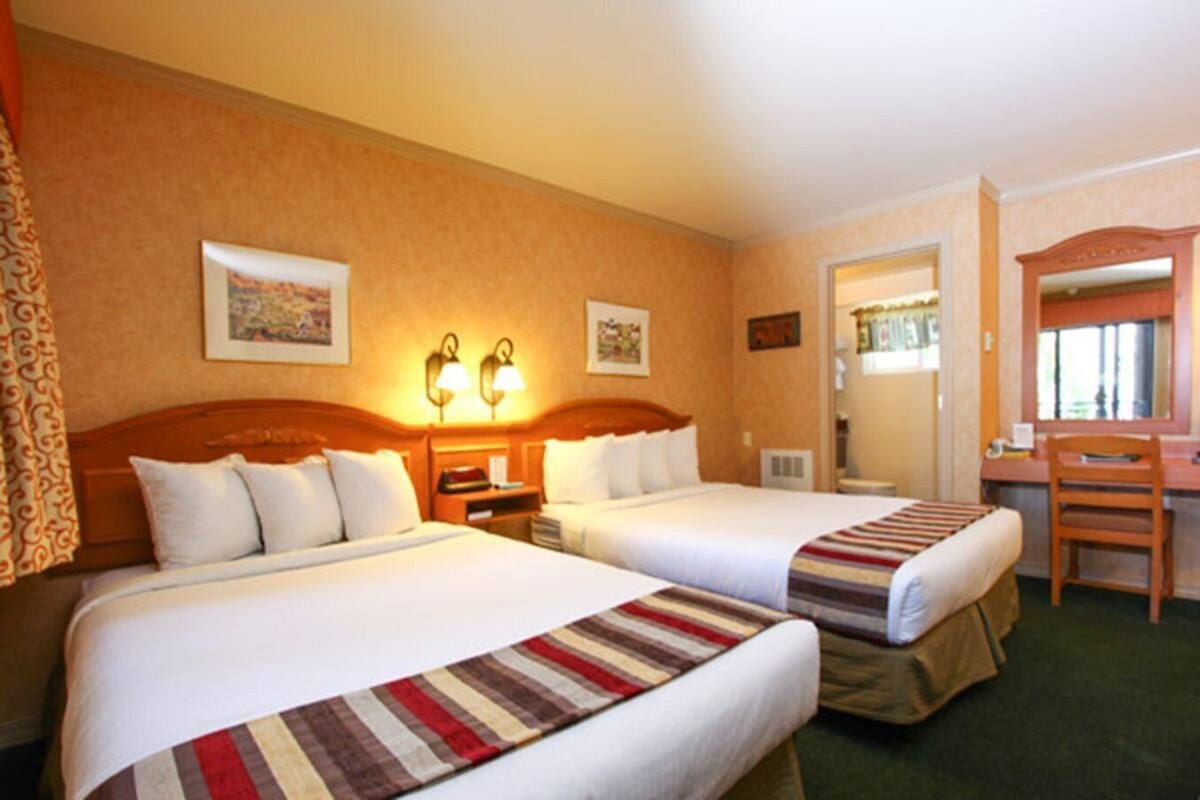 A hotel room with two beds, a desk, a chair, and a mirror.