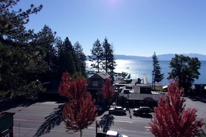 A parking lot with several cars, a building with a sloped roof, and a view of a body of water with mountains in the distance.