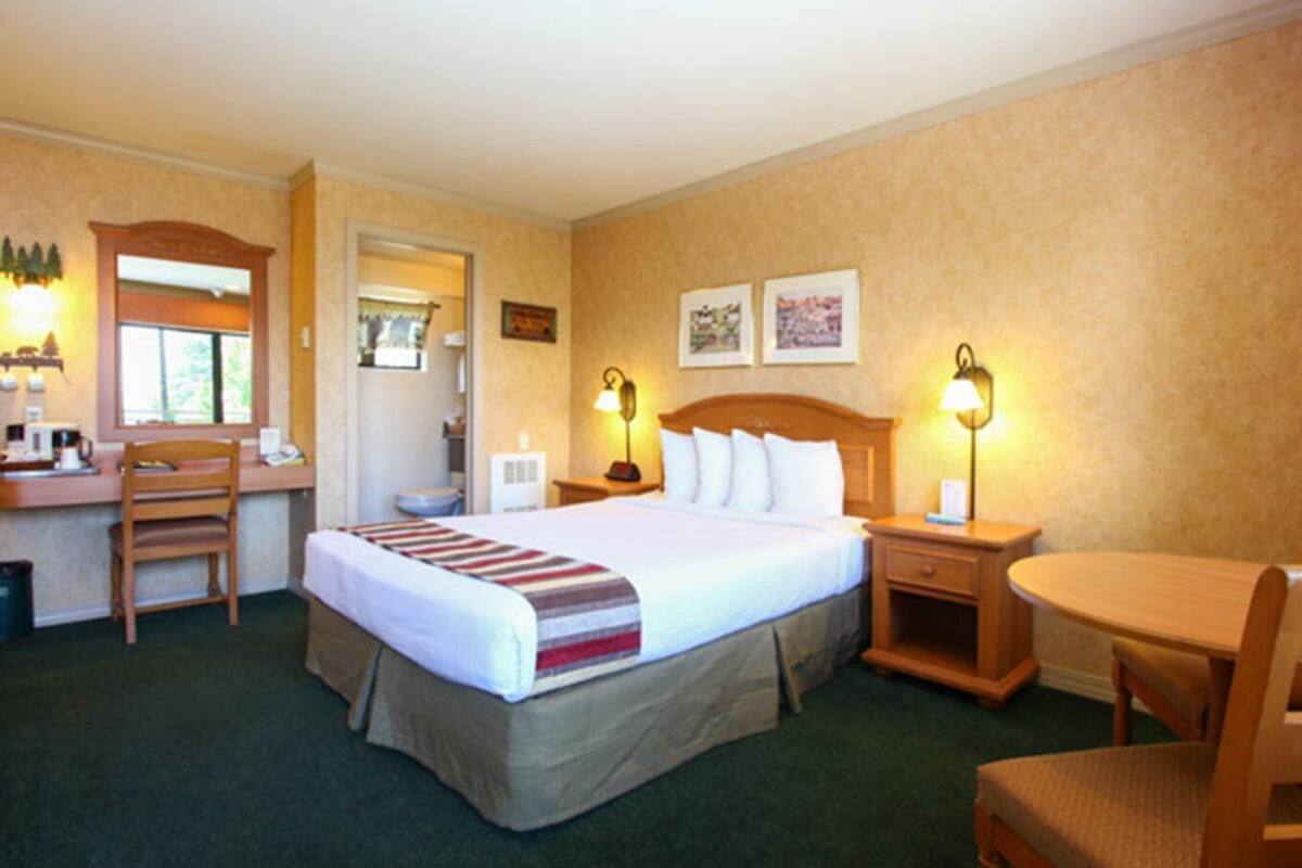 A hotel room with a bed, desk, chair, bedside tables, and a small table.