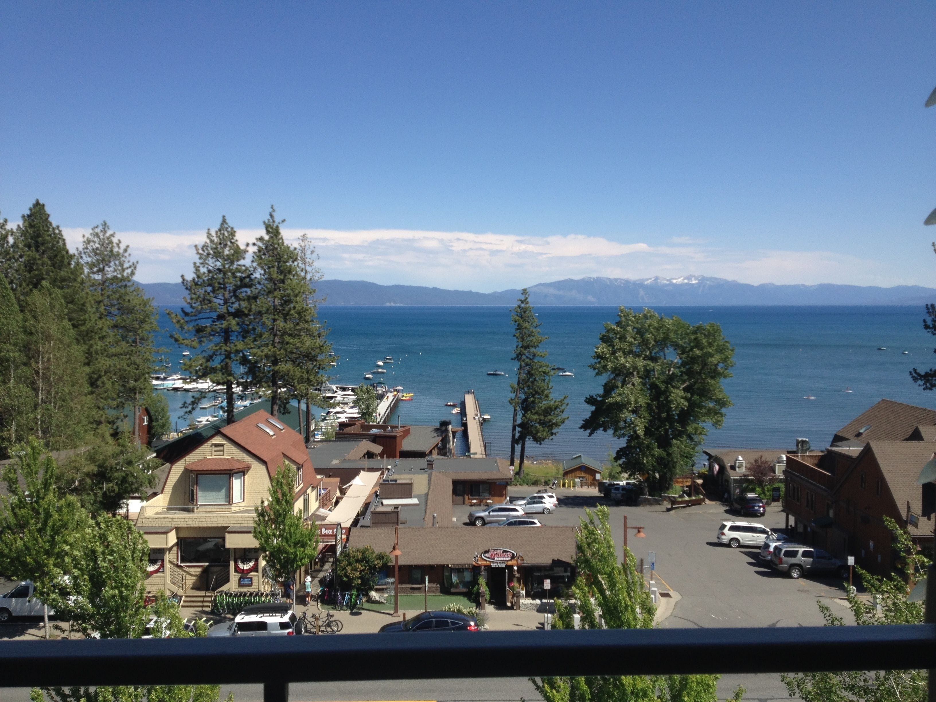 A coastal town with a marina, buildings with sloped roofs, and a clear view of the sea and mountains in the distance.