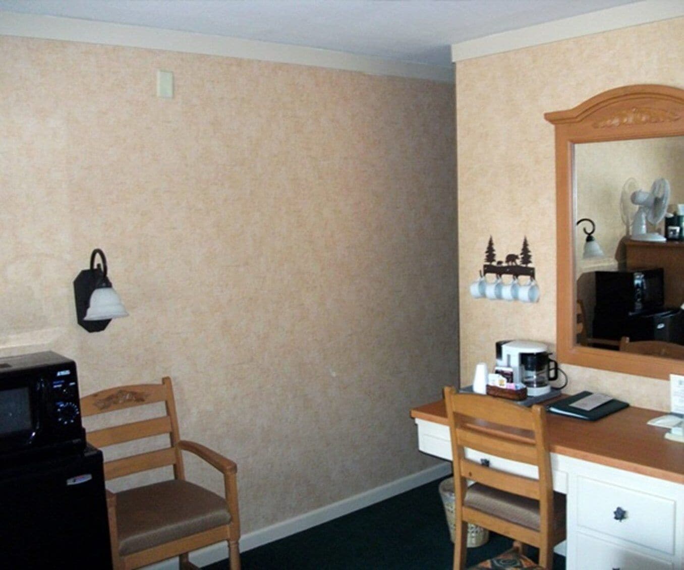 A hotel room with a wooden desk, a chair, a microwave, a coffee maker, and a mirror.