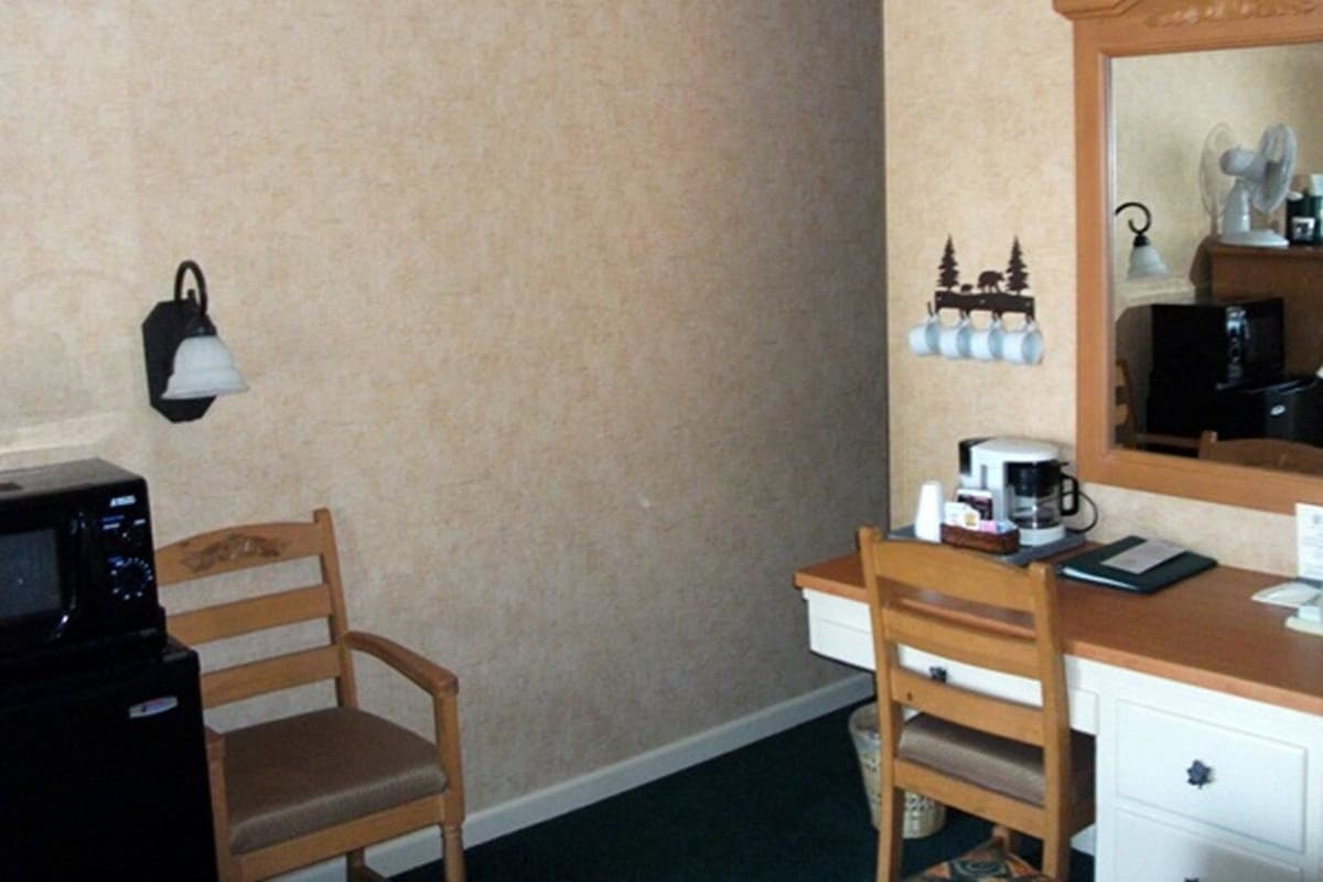 Una habitación de hotel con un escritorio de madera, una silla, un microondas, una cafetera y un espejo.