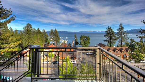 A view from a balcony overlooking a parking lot, a row of houses, and a body of water with mountains in the distance. - Pepper Tree Inn (Tahoe City)