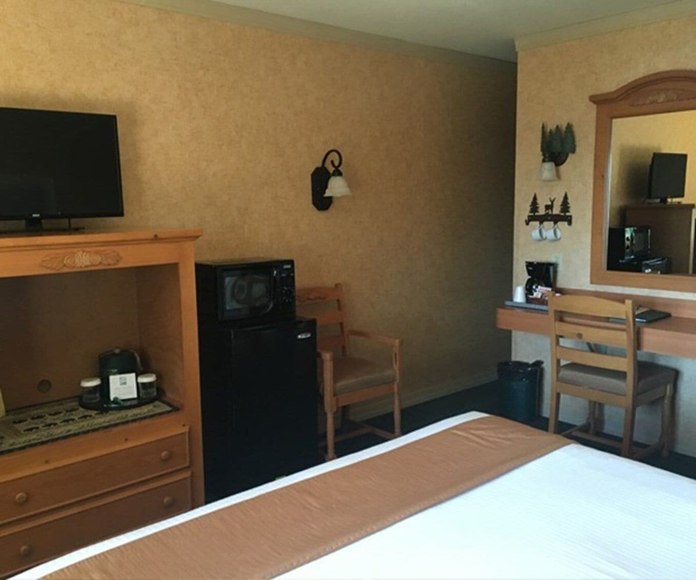 A hotel room with a bed, a desk with a chair, a microwave, a small refrigerator, a television, and a wall-mounted clock.