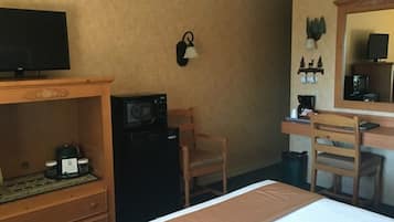 A hotel room with a bed, a desk with a chair, a microwave, a small refrigerator, a television, and a wall-mounted clock.