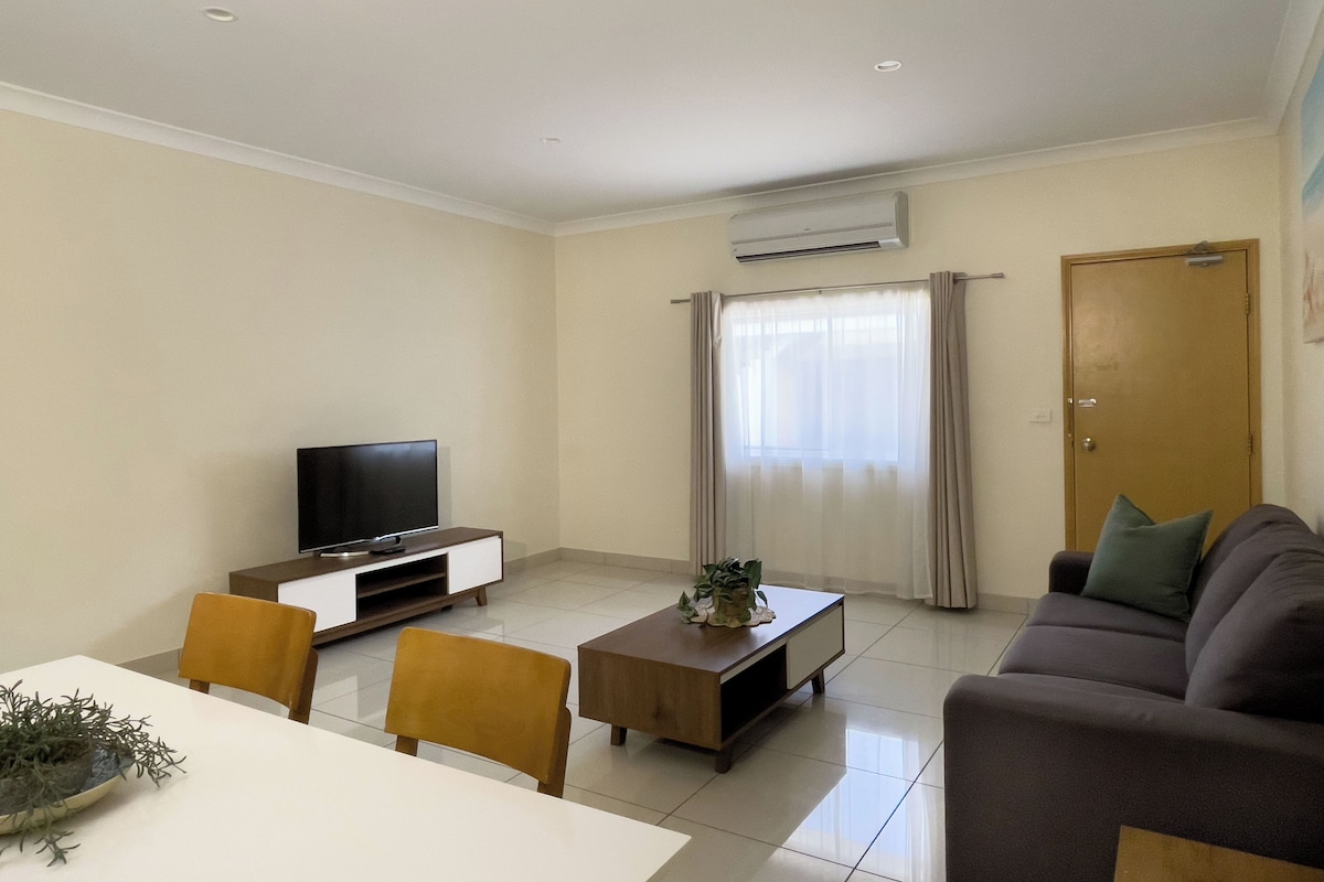A living room with a TV, a sofa, a coffee table, and a dining table with chairs.