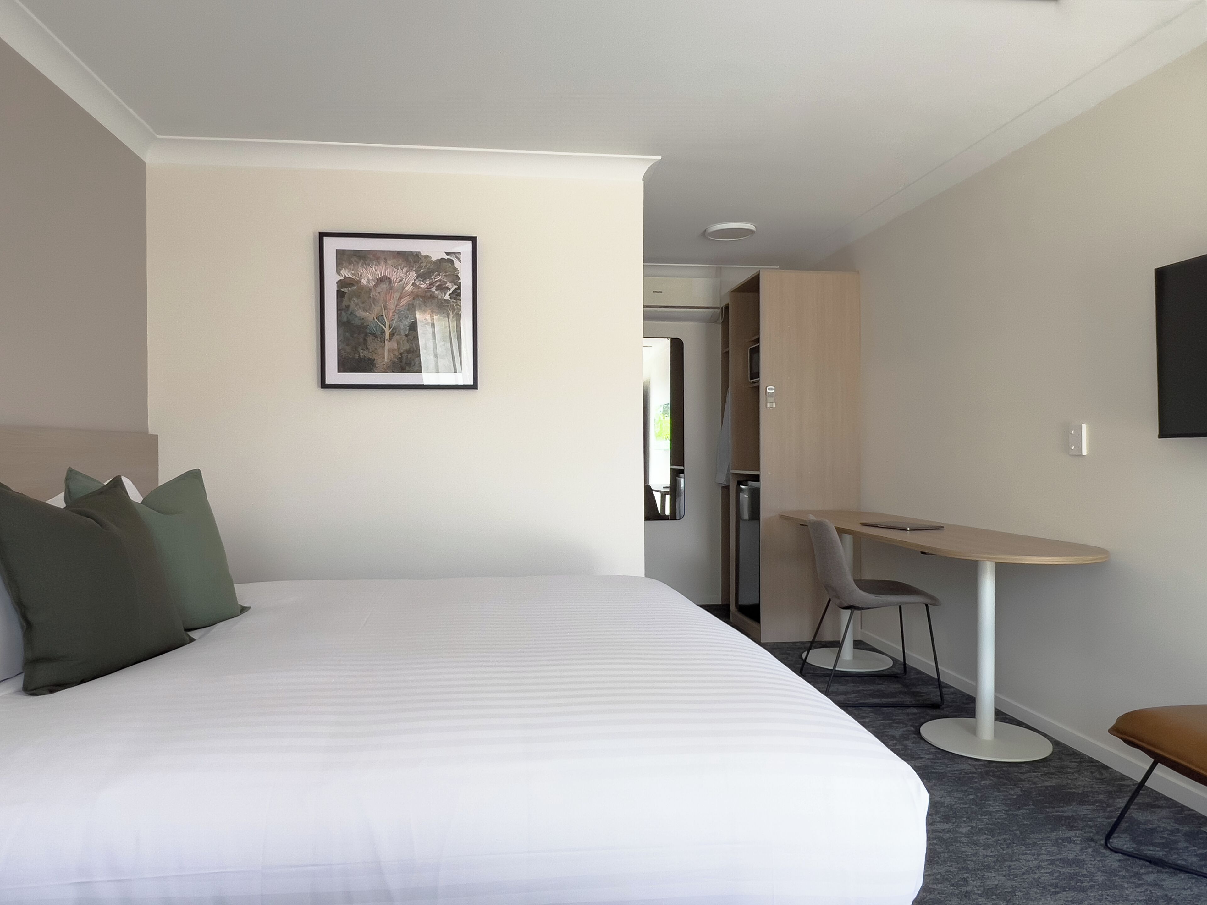 Una habitación de hotel con una cama grande, un escritorio, una silla y un televisor en la pared.