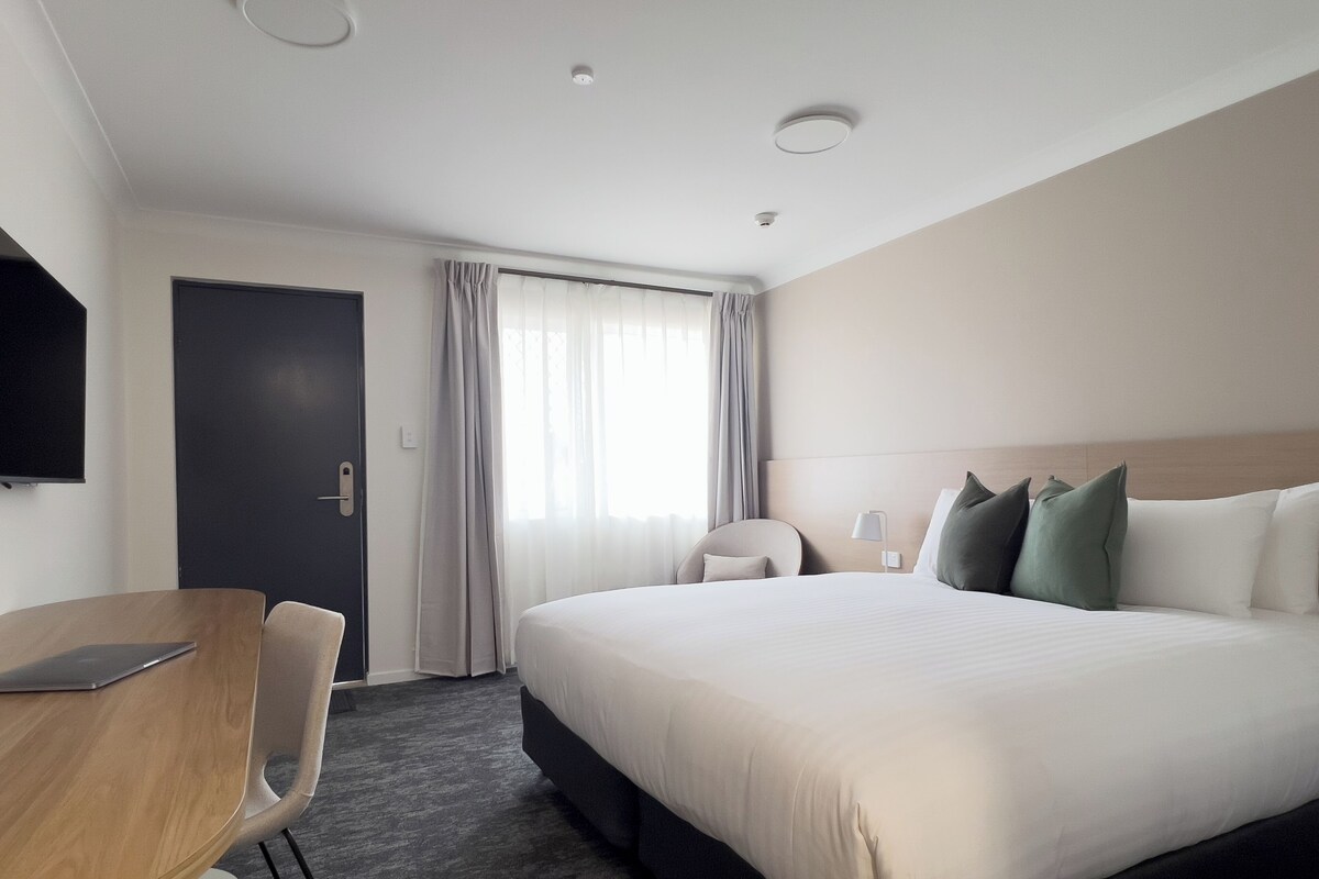 Habitación de hotel con una cama grande, un escritorio, una silla, un televisor y una ventana con cortinas.