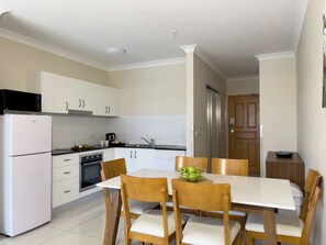 Una cocina moderna con armarios blancos, horno empotrado, microondas y refrigerador de acero inoxidable.