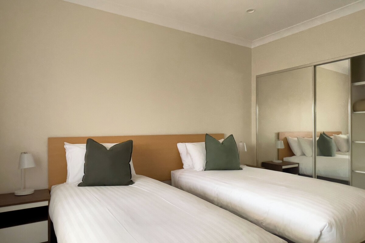 Una habitació d'hotel amb dos llits, una tauleta de nit, una làmpada i un mirall.