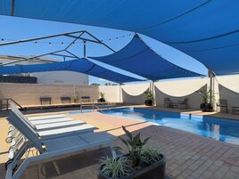 An outdoor swimming pool with sunshade, lounge chairs, and potted plants.