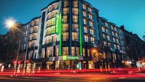 Un hôtel à plusieurs étages, doté d’une façade incurvée, d’une enseigne lumineuse et offrant une vue sur la rue, avec des traînées de lumière.