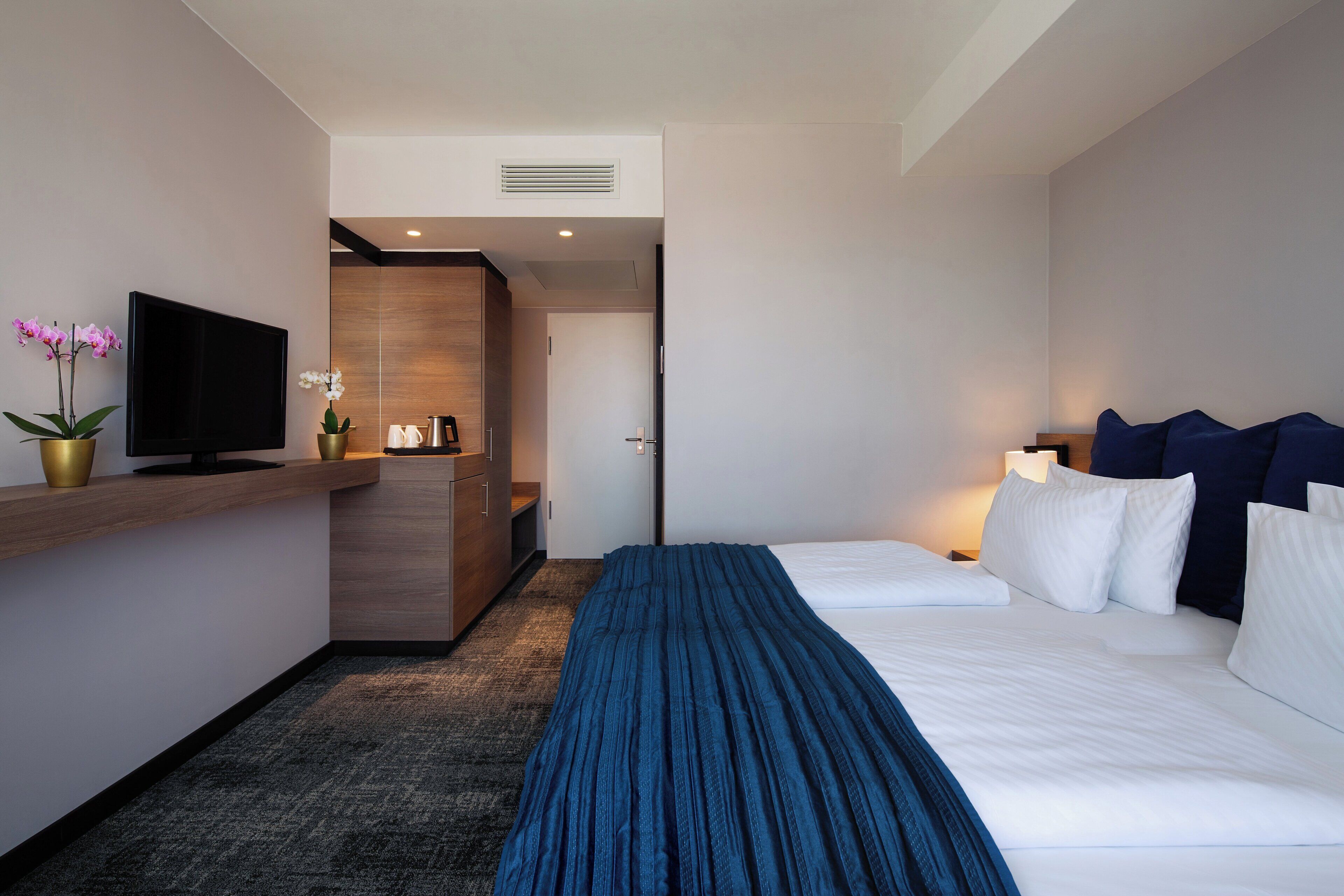 A hotel room with a bed, a TV, a desk, and a bathroom door.