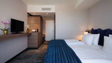 A hotel room with a bed, a TV, a desk, and a bathroom door.
