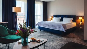 Ein Hotelzimmer mit einem großen Bett, einem Schreibtisch mit Lampe, einem Stuhl und einer Blumenvase.