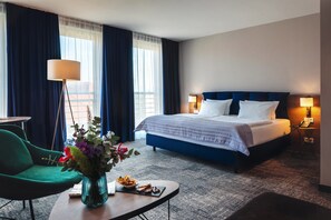 A hotel room with a large bed, a desk with a lamp, a chair, and a vase of flowers. - Holiday Inn Berlin City Center East Prenzlauer Berg by IHG (Berlin)