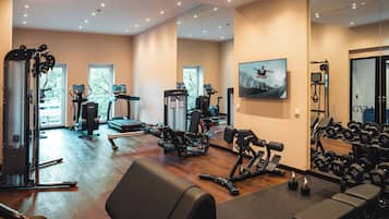 Ein Fitnessraum mit Trainingsgeräten, einem Spiegel und einem Fernsehbildschirm.