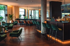 A bar area with high stools, a counter with bottles, and a large window. - Holiday Inn Berlin City Center East Prenzlauer Berg by IHG (Berlin)