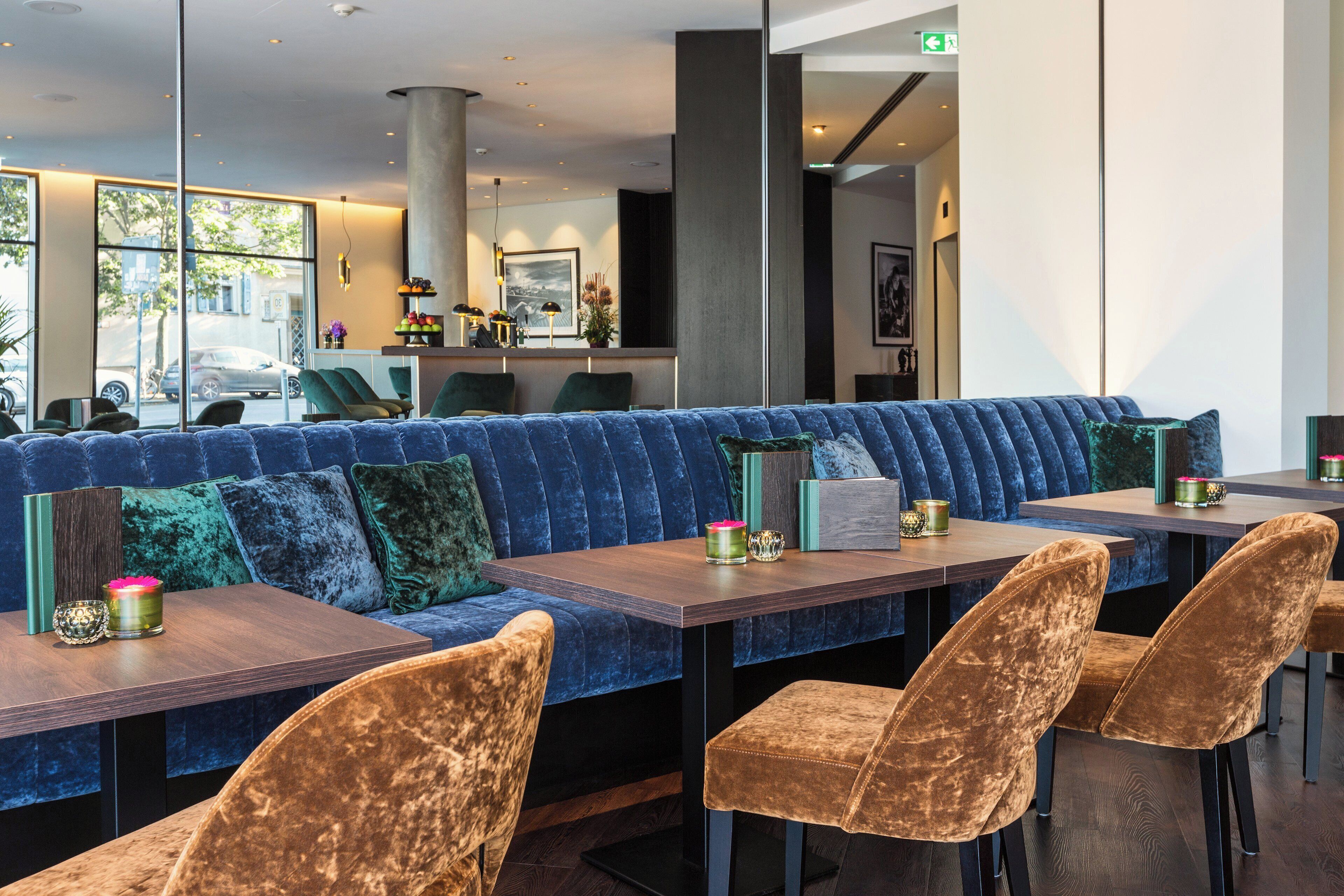 Ein stilvoller Sitzbereich mit einem blau gepolsterten Sofa, Samtstühlen, einem Holztisch und Blick auf die Straße.