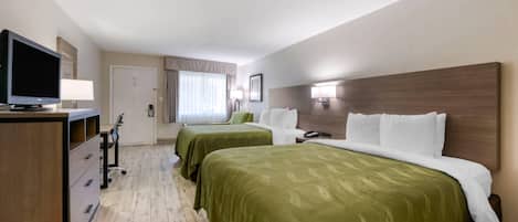 Habitación de hotel con dos camas, un escritorio con televisor y una mesita de noche con lámpara.