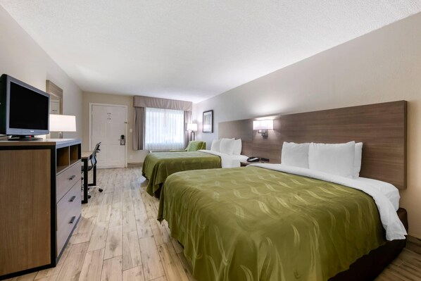 A hotel room with two beds, a desk with a television, and a bedside table with a lamp. - Quality Inn St. Augustine Outlet Mall (St. Augustine)