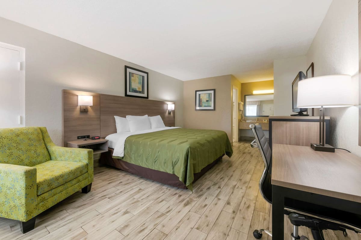A hotel room with a bed, a desk, a chair, and a desk lamp.