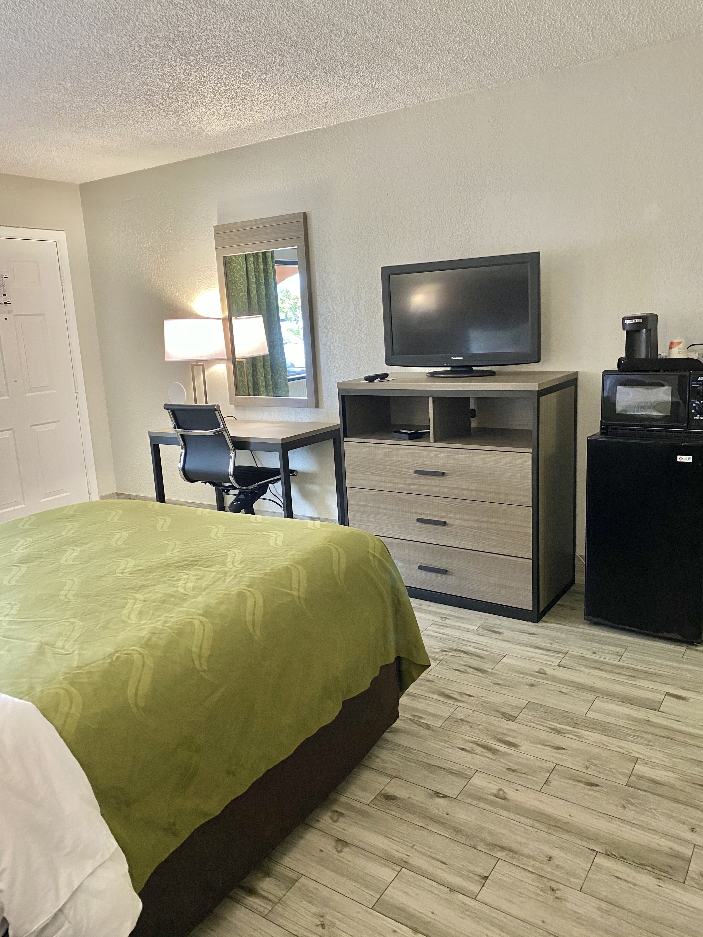Une chambre d’hôtel comprenant un lit, un bureau avec une chaise, une télévision, un minibar et un miroir.