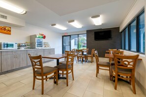 A modern dining area with wooden tables and chairs, a kitchenette, and a large window providing a view of the outside. - Quality Inn St. Augustine Outlet Mall (St. Augustine)