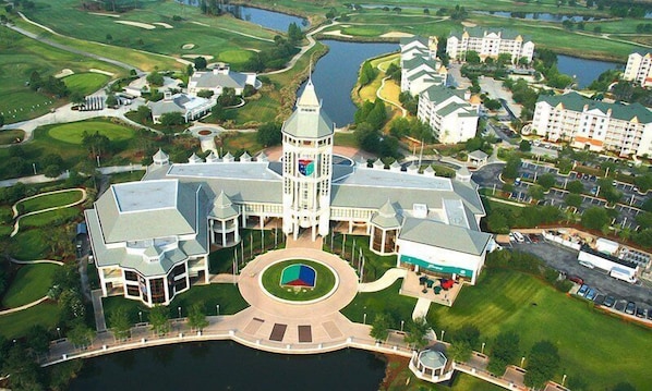 An aerial view of a large, multi-story hotel with a central tower, surrounded by landscaped gardens and a body of water.